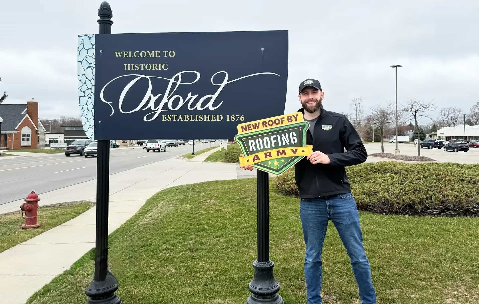 Aaron Scott, owner of Roofing Army, standing in front of the Welcome to Historic Oxford sign in Oxford, Michigan